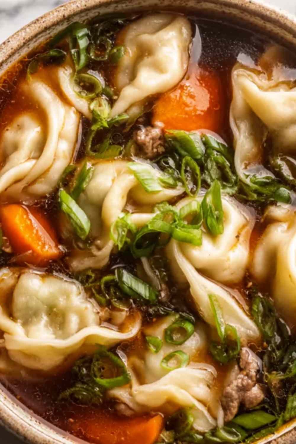 Potsticker soup in a bowl with beef dumplings, fresh greens, and chopped green onion garnish