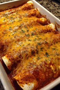 Queso chicken enchiladas topped with melted cheddar and red enchilada sauce fresh from the oven