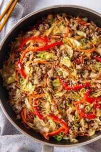 Egg roll in a bowl with ground turkey, cabbage, carrots, and sesame seeds in a large skillet