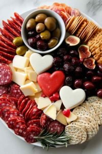 Savory Valentine's Day charcuterie board with heart-shaped brie, prosciutto, salami, grapes, and fresh rosemary on a wooden serving board