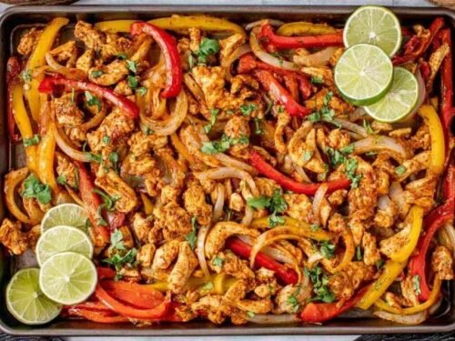 Sheet pan chicken fajitas with colorful bell peppers and caramelized onions on a parchment-lined rimmed baking sheet