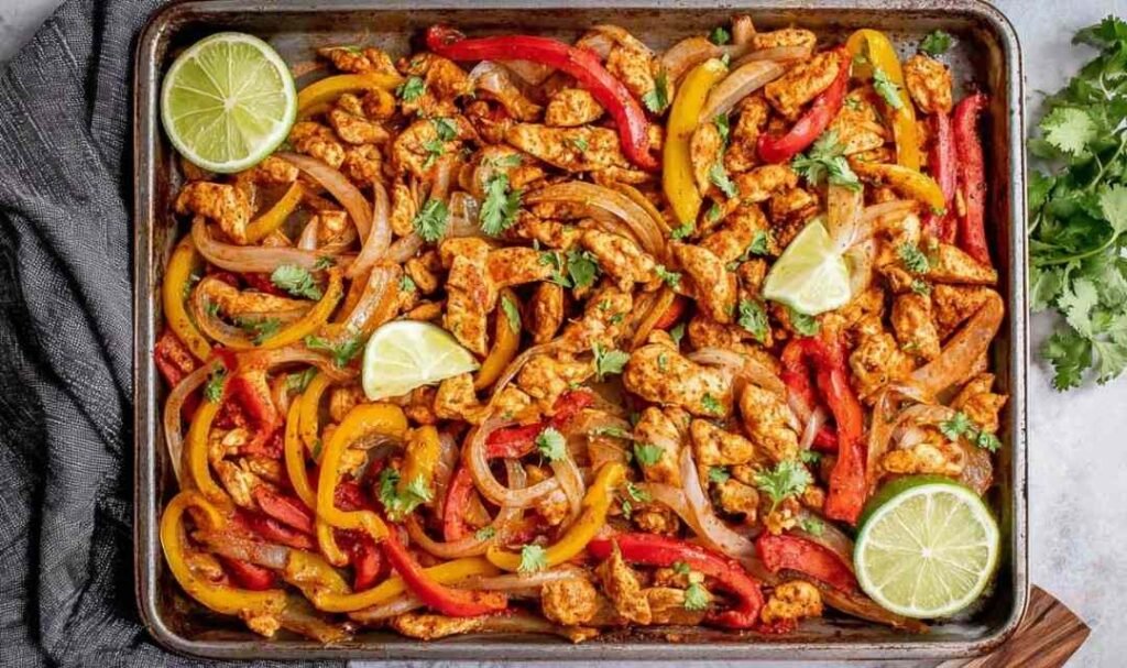 Sheet pan chicken fajitas with colorful bell peppers and caramelized onions on a parchment-lined rimmed baking sheet