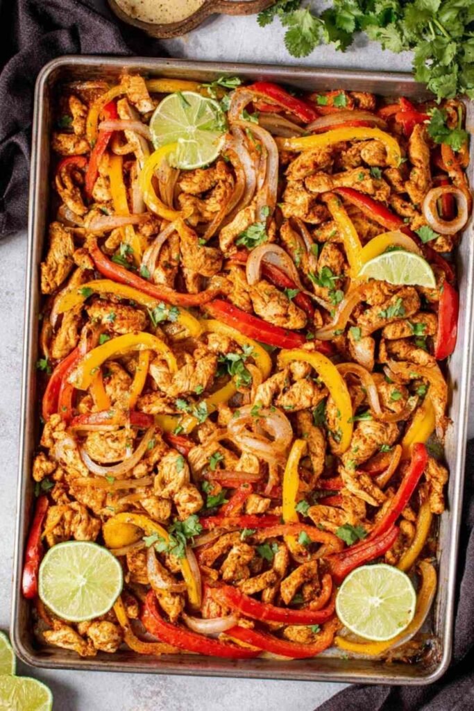 Sheet pan chicken fajitas with colorful bell peppers and caramelized onions on a parchment-lined rimmed baking sheet