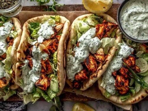 Sheet pan chicken pitas ingredients roasted on a parchment-lined baking sheet with charred bell peppers, zucchini, and cherry tomatoes