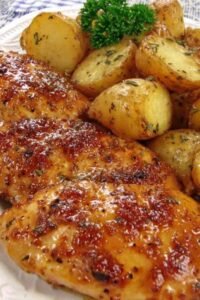Sheet pan chicken and potatoes with honey garlic glaze, golden baked chicken breasts and roasted baby Yukon gold potatoes on a foil-lined baking sheet