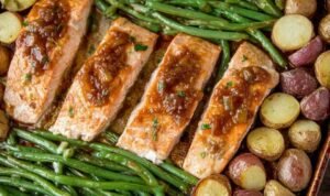 Sheet pan salmon with vegetables showing honey garlic glazed salmon fillets, roasted gold potatoes, and green beans on a parchment-lined baking sheet