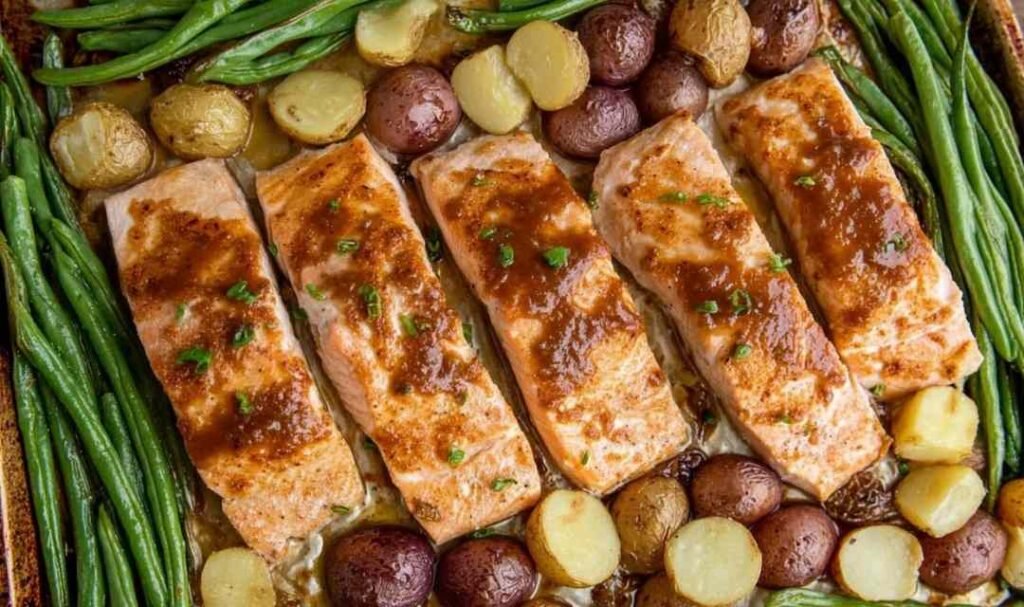 Sheet pan salmon with vegetables showing honey garlic glazed salmon fillets, roasted gold potatoes, and green beans on a parchment-lined baking sheet