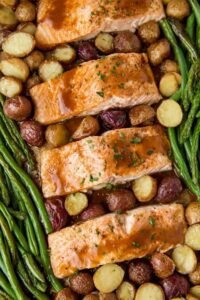 Sheet pan salmon with vegetables showing honey garlic glazed salmon fillets, roasted gold potatoes, and green beans on a parchment-lined baking sheet