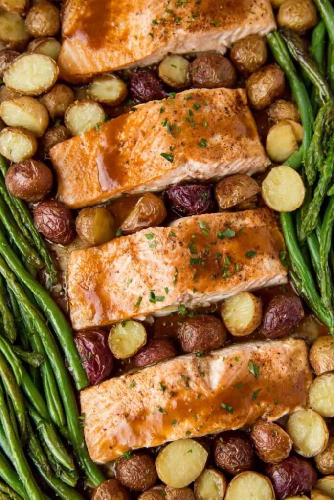 Sheet pan salmon with vegetables showing honey garlic glazed salmon fillets, roasted gold potatoes, and green beans on a parchment-lined baking sheet