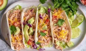 Shredded chicken tacos in flour tortillas topped with avocado, pico de gallo, shredded cheese, and fresh cilantro