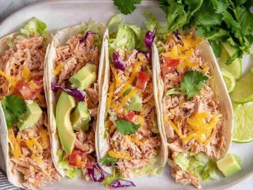 Shredded chicken tacos in flour tortillas topped with avocado, pico de gallo, shredded cheese, and fresh cilantro