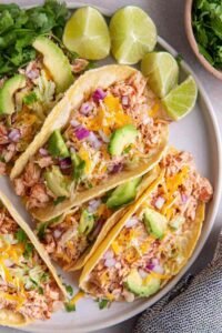 Shredded chicken tacos in flour tortillas topped with avocado, pico de gallo, shredded cheese, and fresh cilantro