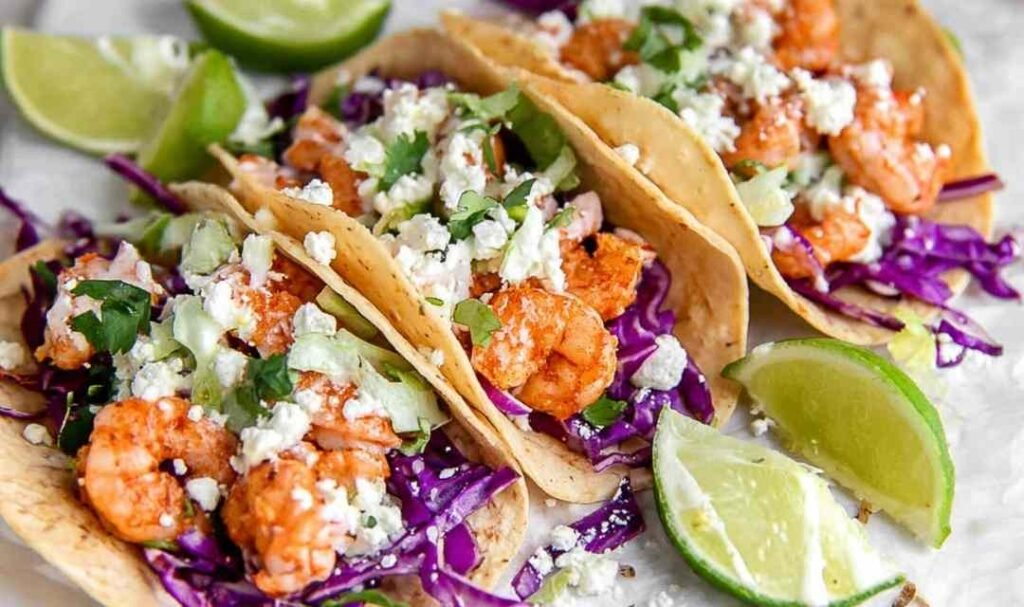 Shrimp Tacos on a plate with crunchy red cabbage, avocado slices, Cotija cheese, and creamy spicy sauce drizzle