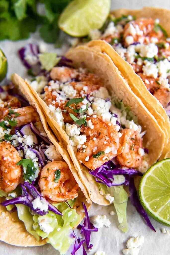 Shrimp Tacos on a plate with crunchy red cabbage, avocado slices, Cotija cheese, and creamy spicy sauce drizzle