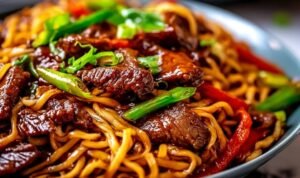 Sticky beef noodles in a bowl with tender flank steak strips, colorful bell peppers, and glossy sweet-savory sauce topped with sesame seeds and green onions