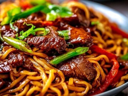 Sticky beef noodles in a bowl with tender flank steak strips, colorful bell peppers, and glossy sweet-savory sauce topped with sesame seeds and green onions