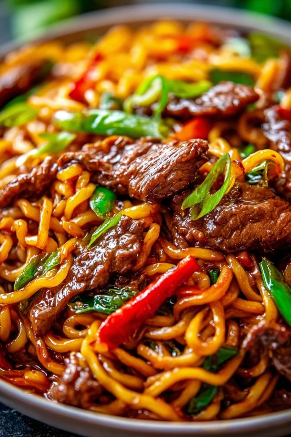 Sticky beef noodles in a bowl with tender flank steak strips, colorful bell peppers, and glossy sweet-savory sauce topped with sesame seeds and green onions