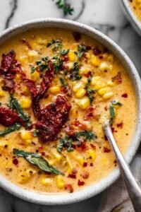Sun-dried tomato corn chowder in a white bowl garnished with fresh basil and a swirl of cream
