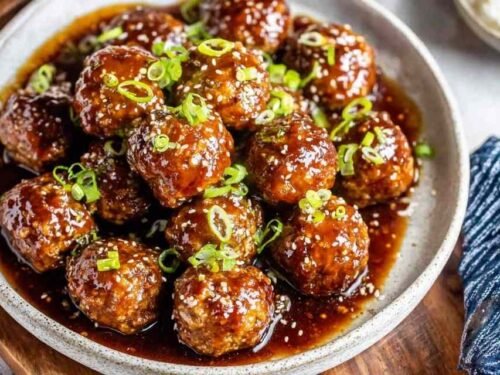 A bowl of sweet and sour meatballs over steamed white rice drizzled with sticky hoisin-honey glaze and garnished with sliced green onions