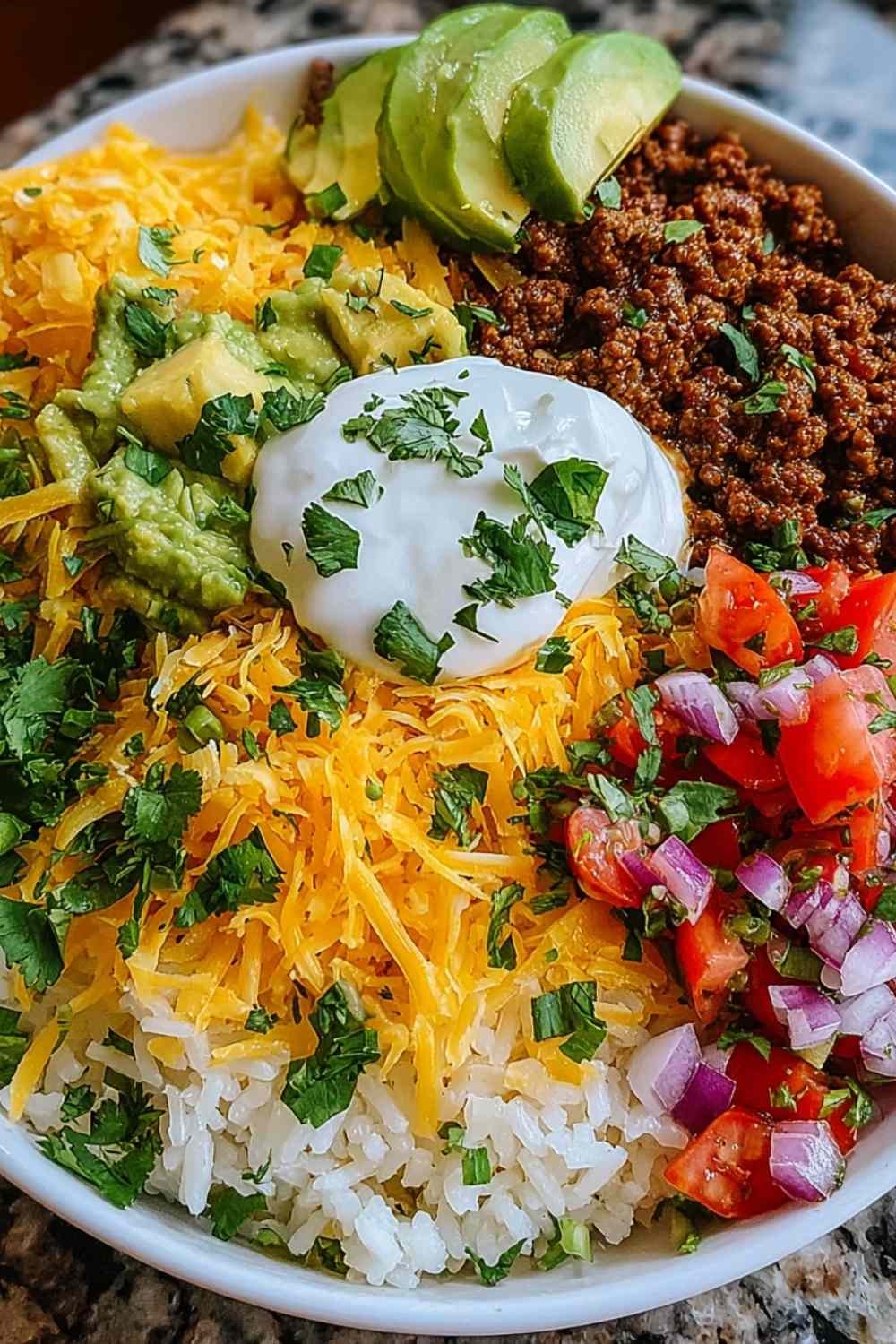 Taco rice bowl with seasoned ground beef, black beans, corn, shredded cheddar, and fresh tomatoes