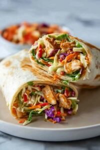 Thai Chicken Wrap with Crunchy Asian Slaw sliced in half and served on a wooden board with peanut sauce drizzle
