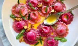 Valentine's Day ravioletti with pink beet pasta served in silky butter sauce with toasted walnuts and fresh mint and dill on a white plate