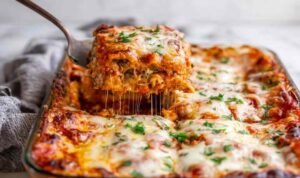 Best Vegetable Lasagna A slice of vegetable lasagna being lifted from a white baking dish showing distinct layers of creamy ricotta, marinara sauce, sauteed vegetables, and melted mozzarella cheese