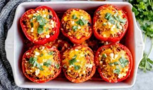 Six colorful vegetarian stuffed peppers in a baking dish with melted cheese and fresh cilantro garnish