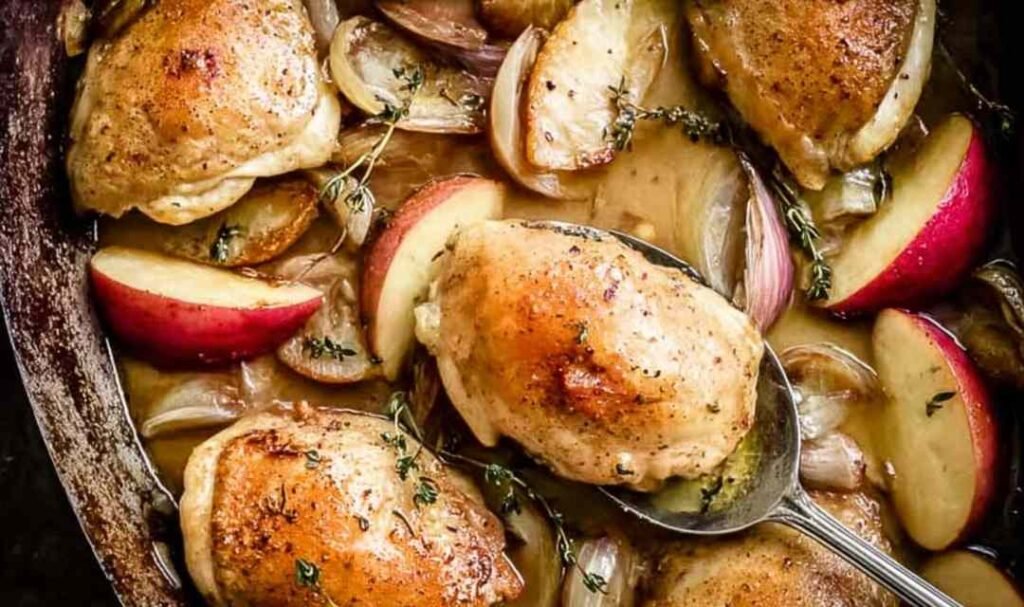 Baked apple chicken on a sheet pan with caramelized apple slices, onions, and fresh thyme garnish