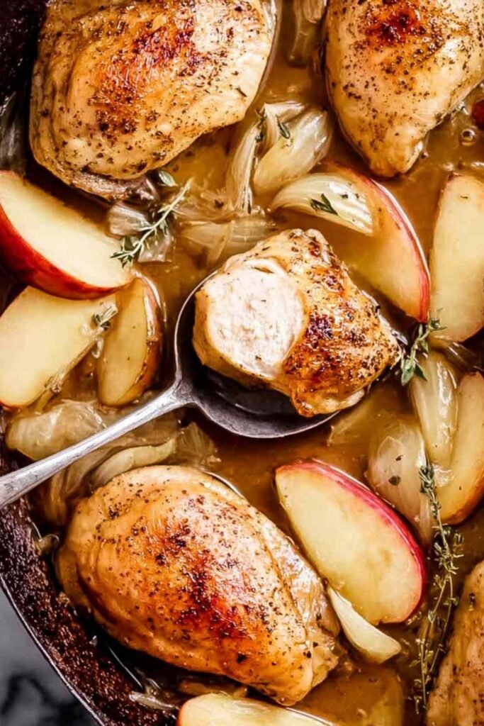 Baked apple chicken on a sheet pan with caramelized apple slices, onions, and fresh thyme garnish