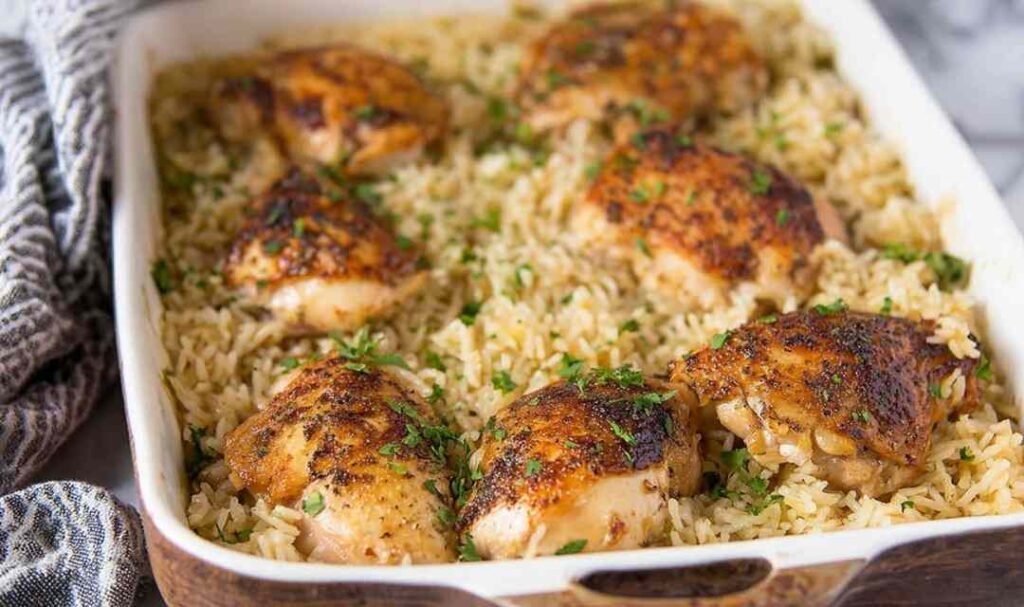 Baked chicken and rice casserole in a white 9x13 dish with golden seasoned chicken thighs over creamy rice, garnished with fresh parsley