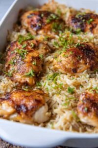 Baked chicken and rice casserole in a white 9x13 dish with golden seasoned chicken thighs over creamy rice, garnished with fresh parsley