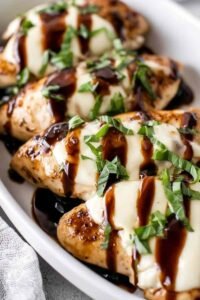 Balsamic baked chicken breast with mozzarella cheese and cherry tomatoes served in a white baking dish