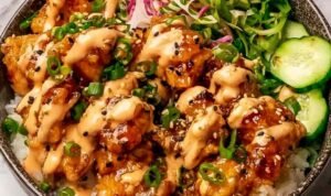 Bang bang chicken bowl with crispy chicken, jasmine rice, cucumber, carrots, and bang bang sauce drizzle overhead