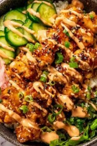 Bang bang chicken bowl with crispy chicken, jasmine rice, cucumber, carrots, and bang bang sauce drizzle overhead