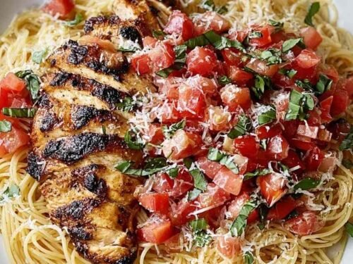 Bruschetta Chicken Pasta with sliced baked chicken breast, fresh tomato basil bruschetta topping, and grated Parmesan in a white bowl