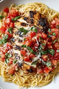 Bruschetta Chicken Pasta with sliced baked chicken breast, fresh tomato basil bruschetta topping, and grated Parmesan in a white bowl