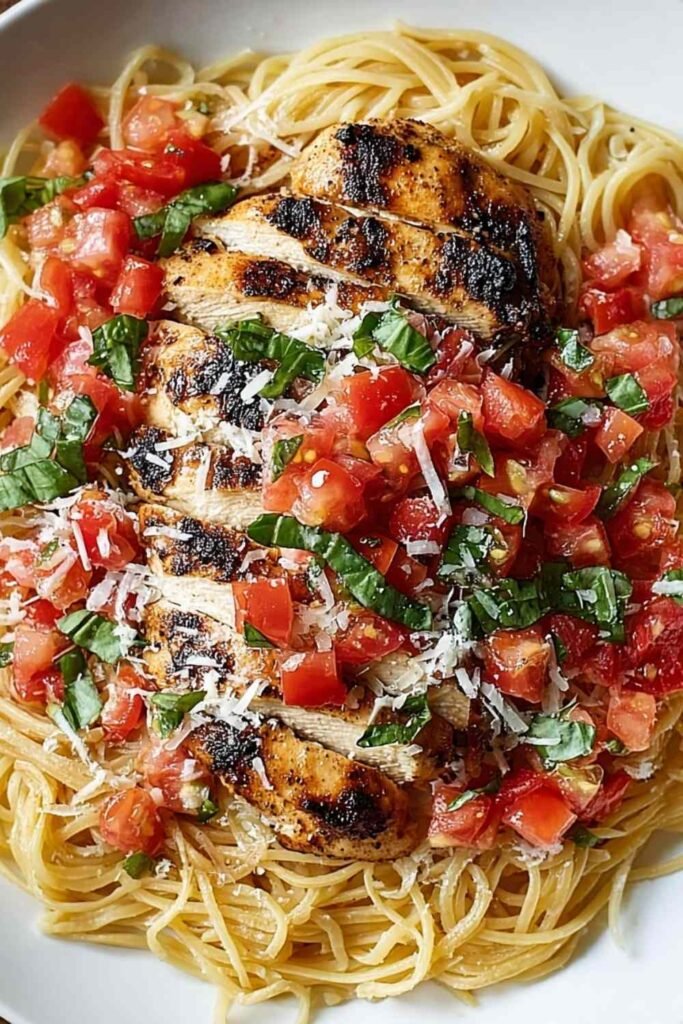 Bruschetta Chicken Pasta with sliced baked chicken breast, fresh tomato basil bruschetta topping, and grated Parmesan in a white bowl