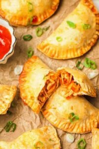 Golden baked chicken empanadas on a parchment-lined baking sheet fresh from the oven