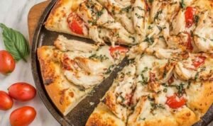 Chicken margherita pizza on a pizza stone with golden crust, melted fresh mozzarella, grilled chicken, and fresh basil leaves