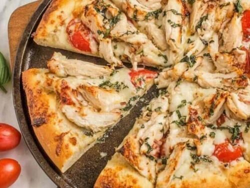 Chicken margherita pizza on a pizza stone with golden crust, melted fresh mozzarella, grilled chicken, and fresh basil leaves