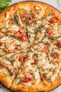 Chicken margherita pizza on a pizza stone with golden crust, melted fresh mozzarella, grilled chicken, and fresh basil leaves