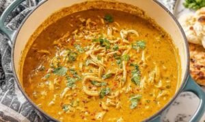 A bowl of homemade chicken mulligatawny soup topped with roasted cashews and fresh cilantro on a wooden table