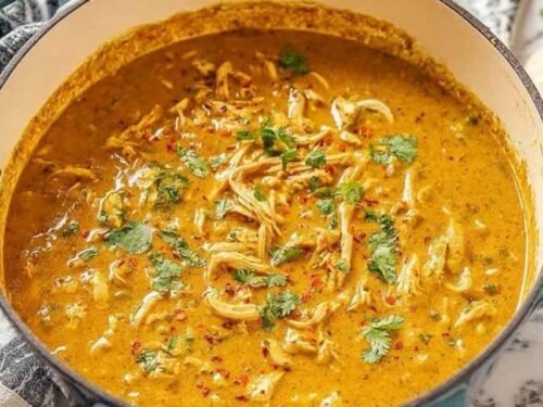 A bowl of homemade chicken mulligatawny soup topped with roasted cashews and fresh cilantro on a wooden table