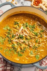 A bowl of homemade chicken mulligatawny soup topped with roasted cashews and fresh cilantro on a wooden table