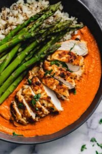 Chicken romesco recipe with juicy baked chicken breast topped with smoky roasted red pepper almond sauce on a white dinner plate