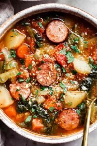 A bowl of hearty chicken sausage stew with white beans, potatoes, and spinach topped with Parmesan cheese