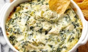A baking dish of homemade chicken spinach artichoke dip recipe with bubbly golden top served with tortilla chips