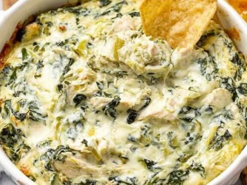 A baking dish of homemade chicken spinach artichoke dip recipe with bubbly golden top served with tortilla chips