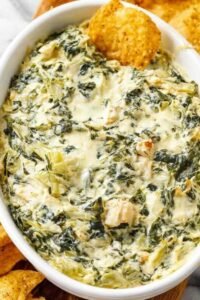 A baking dish of homemade chicken spinach artichoke dip recipe with bubbly golden top served with tortilla chips